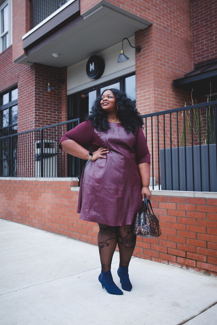 Plussize Blogger wearing leather dress. Color is maroon. Woman has curly hair. 