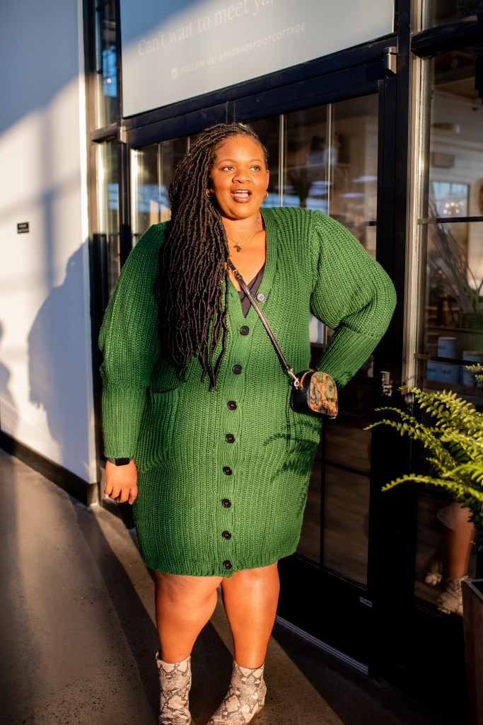 Woman standing in green sweater dress and boots  